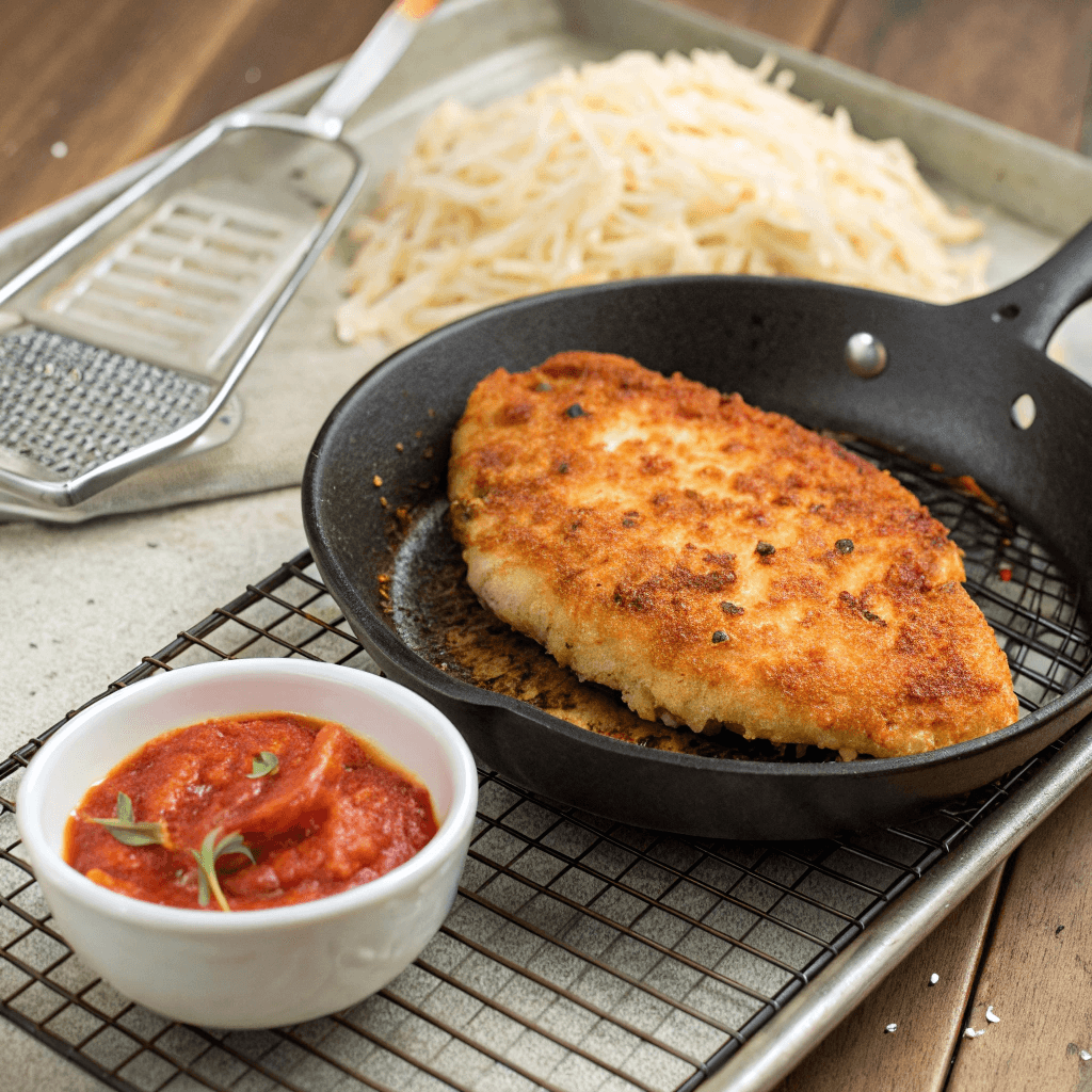  A crispy breaded chicken cutlet resting on a wire rack after frying, ready to be used in a Chicken Parmesan Sandwich